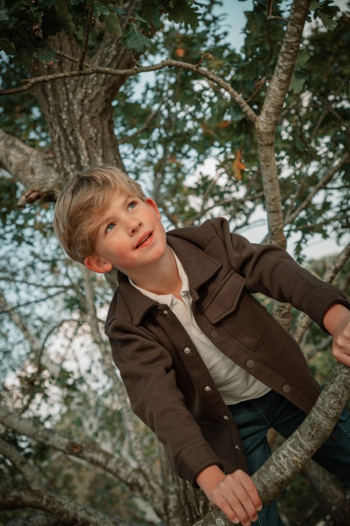 Jongen kijkt omhoog tussen de bomen tijdens een kinderfotoshoot in de buitenlucht.